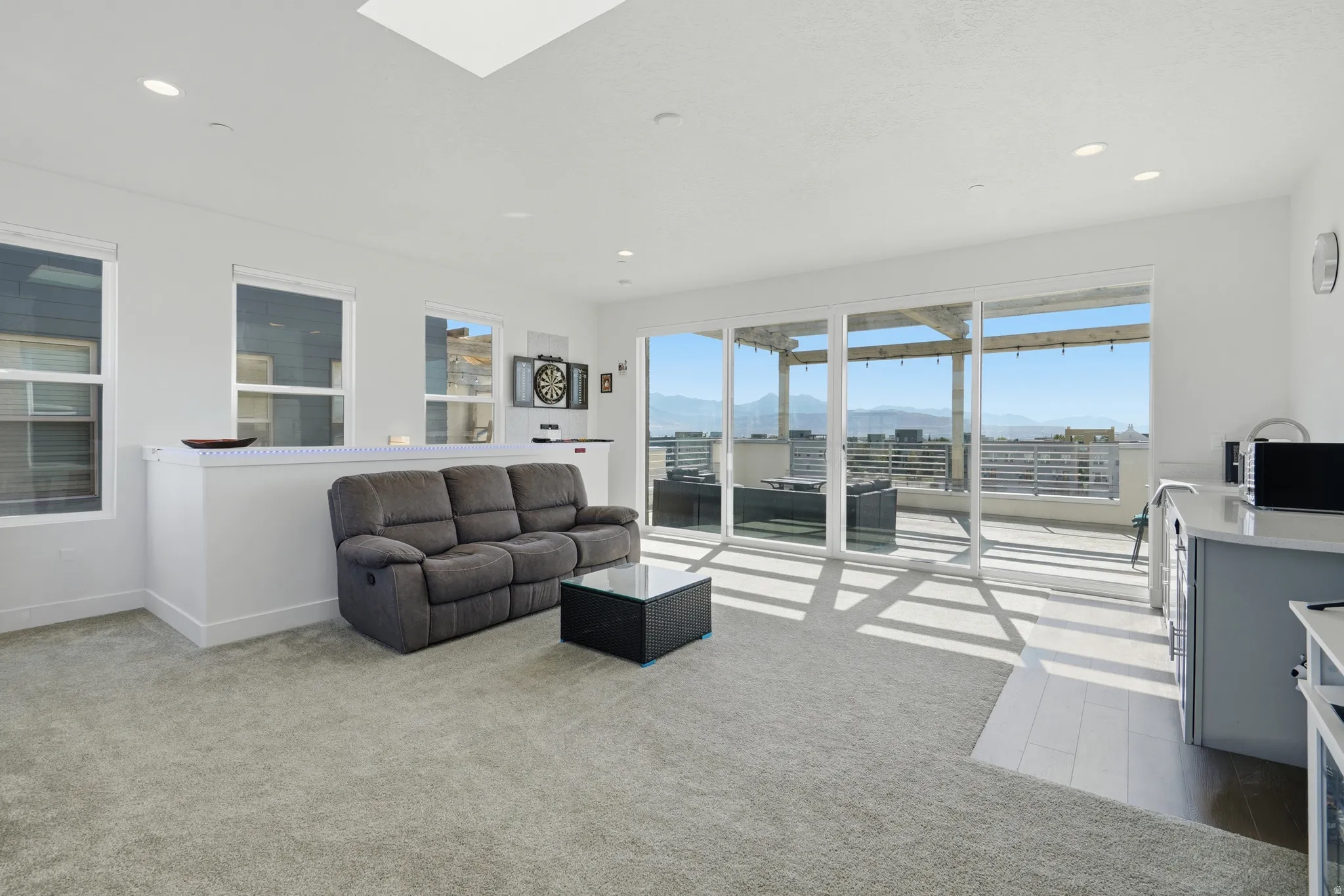 Expansive sliding glass doors opening to a large balcony, multiple windows, a ceiling skylight, and recessed lighting