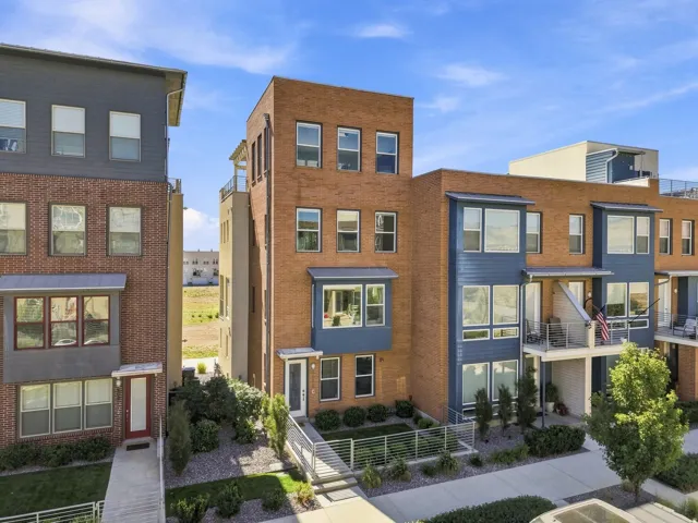 Multi-story facade featuring brick and horizontal siding, multiple balconies with metal railings, a flat roofline, and integrated landscaping with planted shrubs