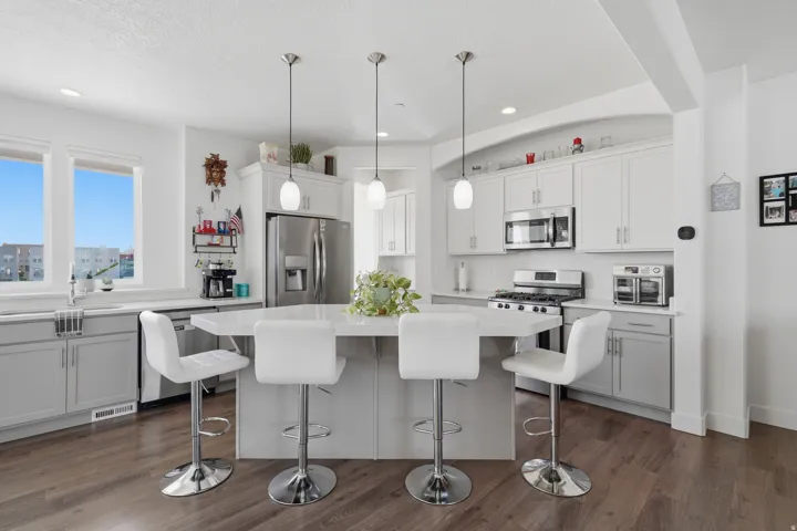 Kitchen featuring a central island with pendant lighting, stainless steel appliances, dual-tone cabinetry, and wood-finish flooring