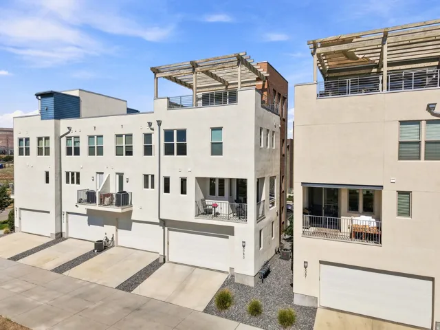 Contemporary multi-story exterior with integrated garages, private balconies, and rooftop deck with a pergola