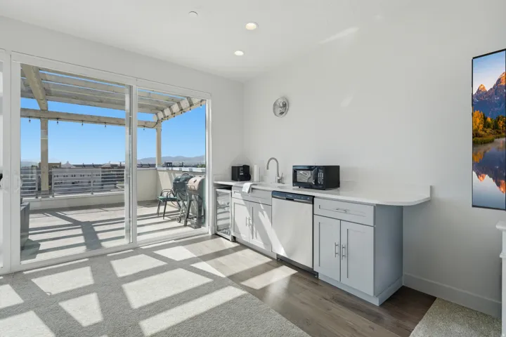 Sliding glass doors opening to a pergola-covered outdoor space, built-in wet bar with stainless steel dishwasher, integrated sink, and light gray cabinetry, and recessed lighting