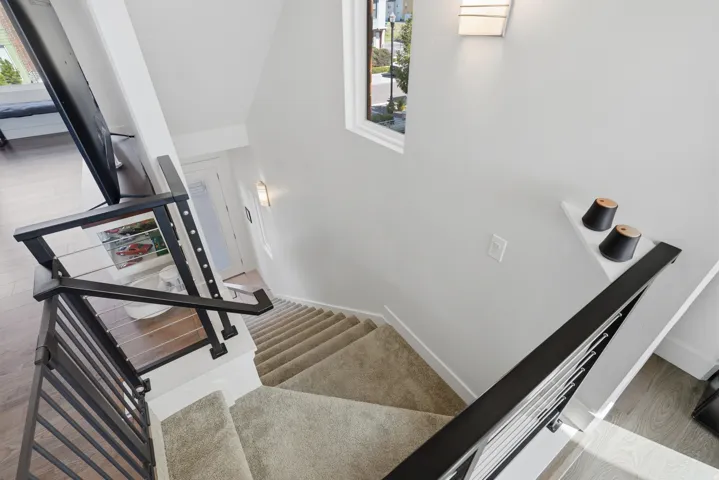 Modern black metal stair railing with cable infill, white walls, carpeted stairs, and wood-finish flooring