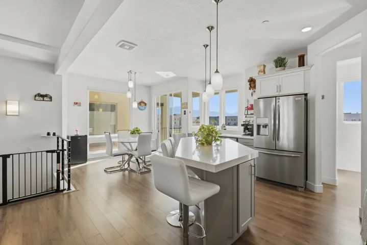 Open-concept kitchen and dining area featuring wood-finish flooring, a kitchen island with pendant lighting, stainless steel appliances, and white cabinetry