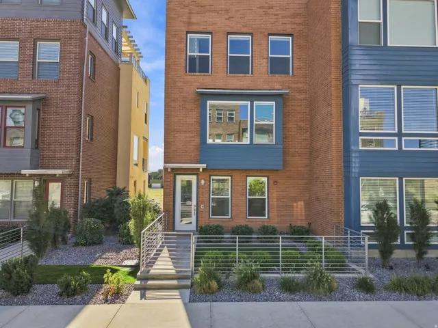 Brick exterior with modern blue accent siding, multiple windows across three levels, concrete entrance with metal railings, and landscaped front yard