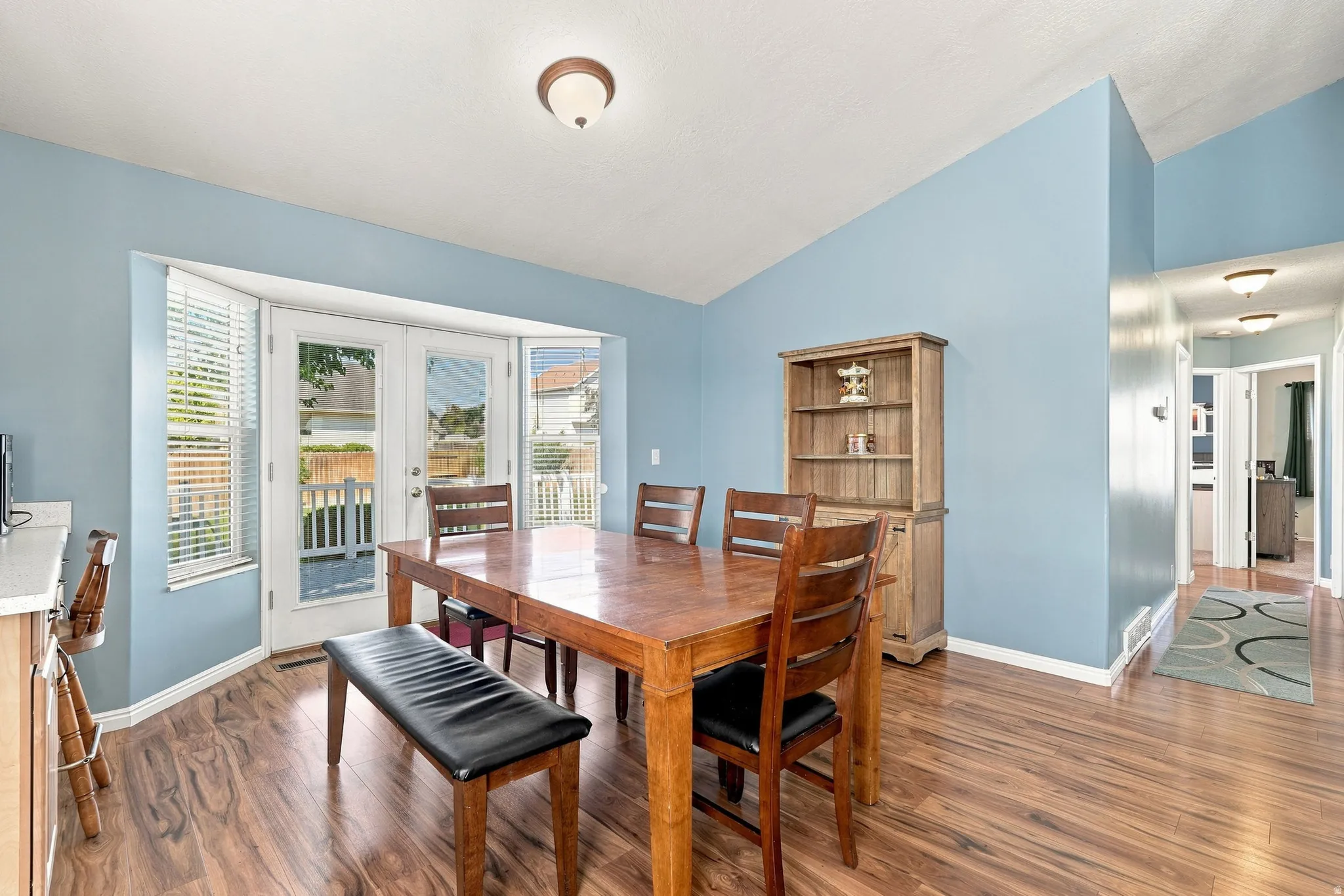 Wood-finish flooring throughout, vaulted ceiling, bay window with French doors, and built-in shelving unit