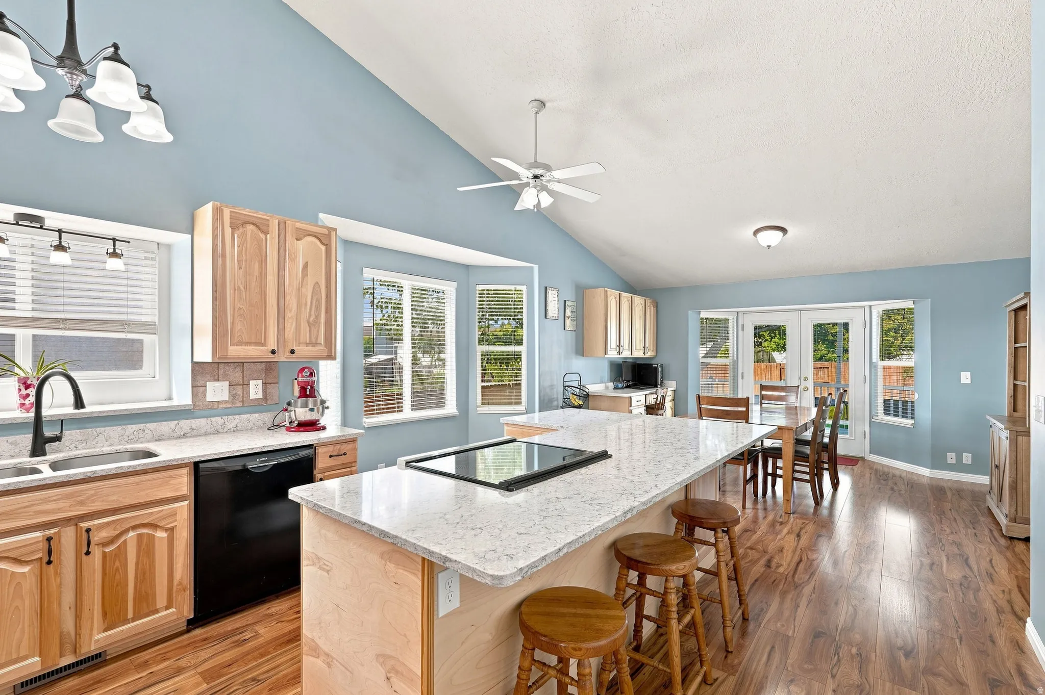 Kitchen featuring vaulted ceilings, wood-finish flooring, light wood cabinetry, white stone countertops, and a central island with an integrated cooktop