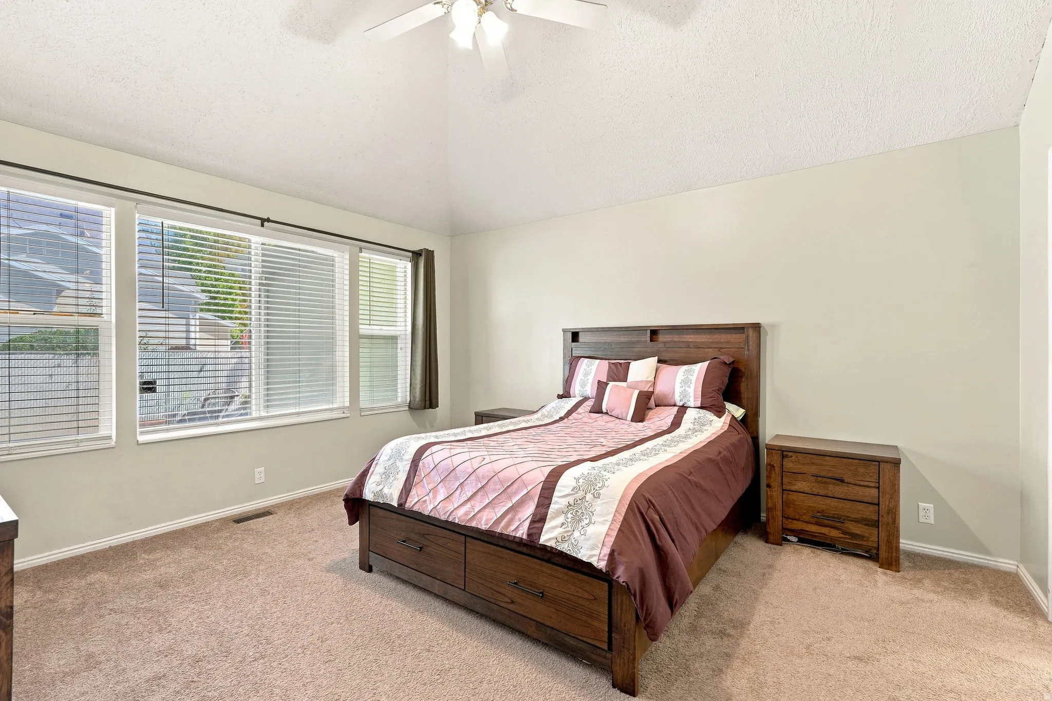 Vaulted ceiling with a ceiling fan, light-toned wall paint, large windows with blinds, and neutral carpet flooring