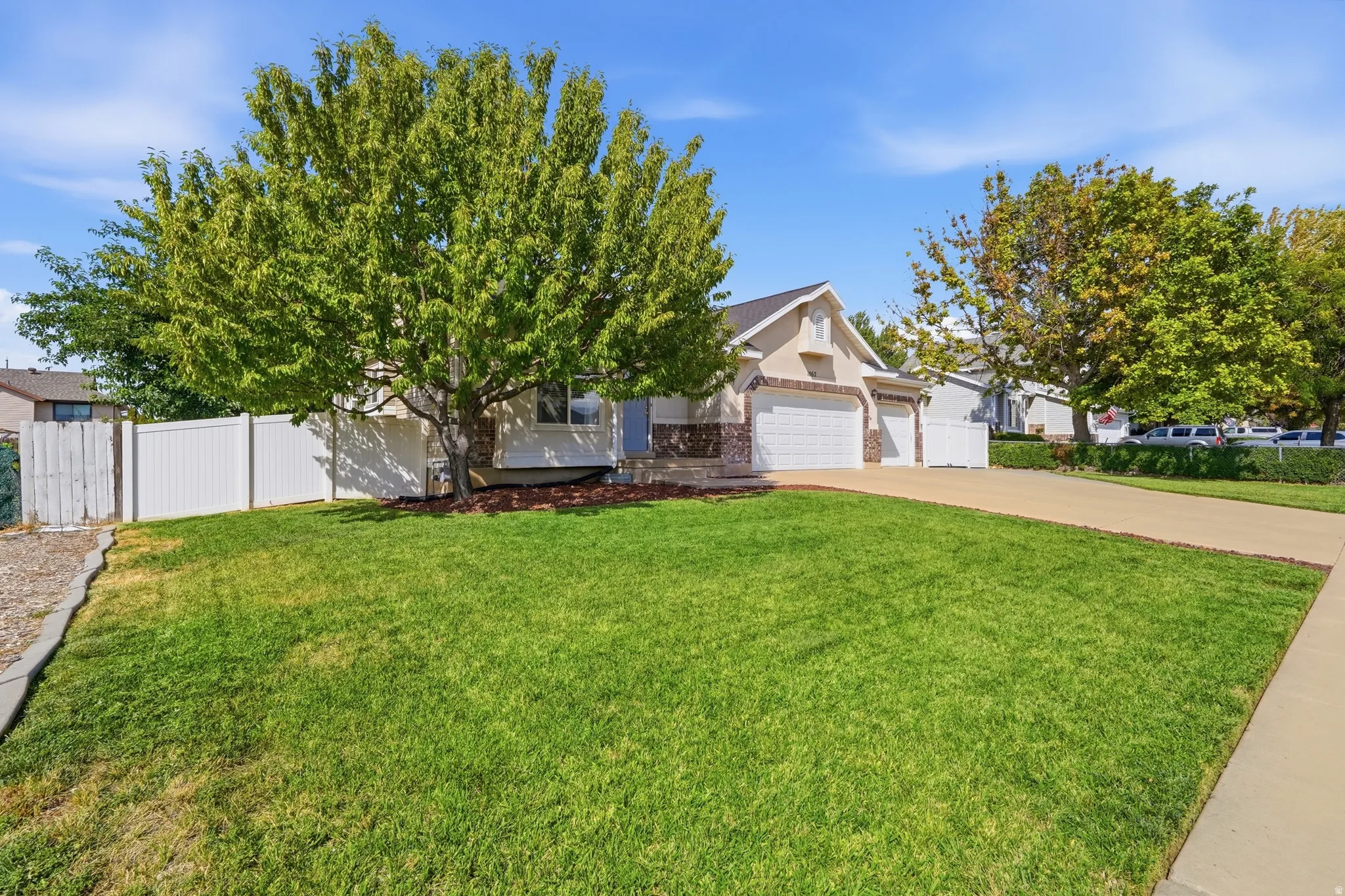 Two-car garage, manicured lawn, paved driveway, mature trees, and privacy fencing