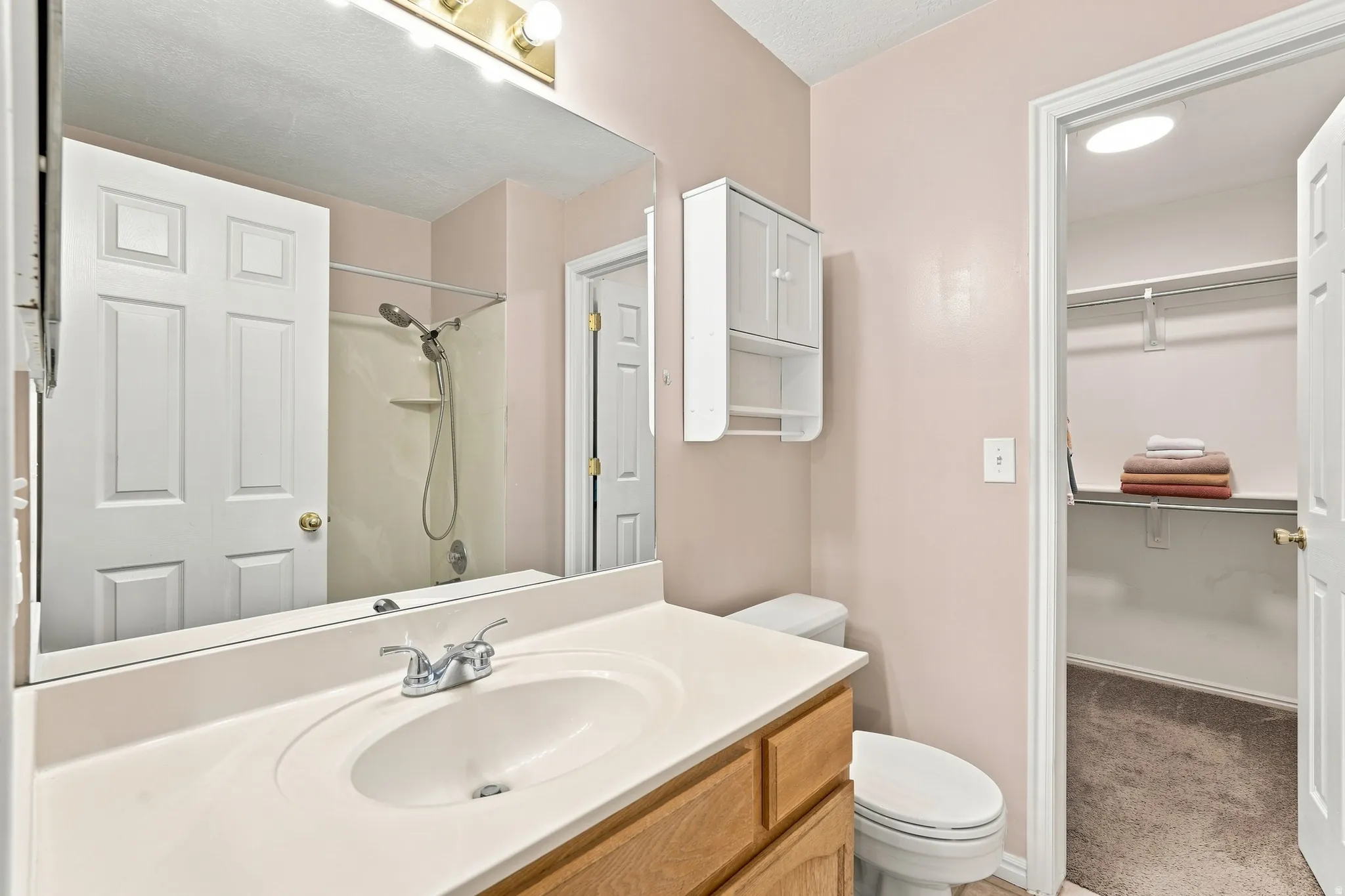 Spacious bathroom featuring a wood-finish vanity with an integrated sink, a large wall-mounted mirror, and an adjacent walk-in closet with shelving and hanging rods