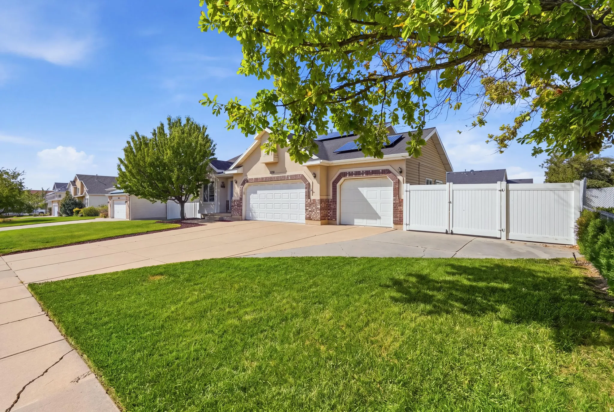 Tan stucco and brick exterior, two-car garage, white privacy fence, solar panels, and a concrete driveway
