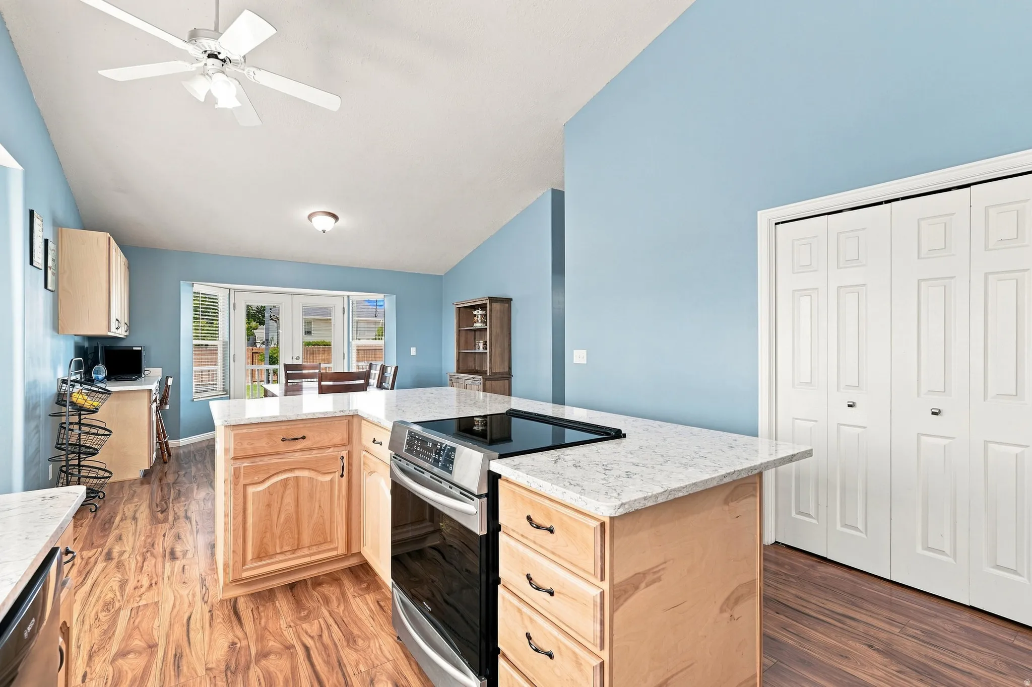 Kitchen island with built-in stainless steel range, light wood-finish cabinetry, light-colored countertops, wood-finish flooring, and vaulted ceiling