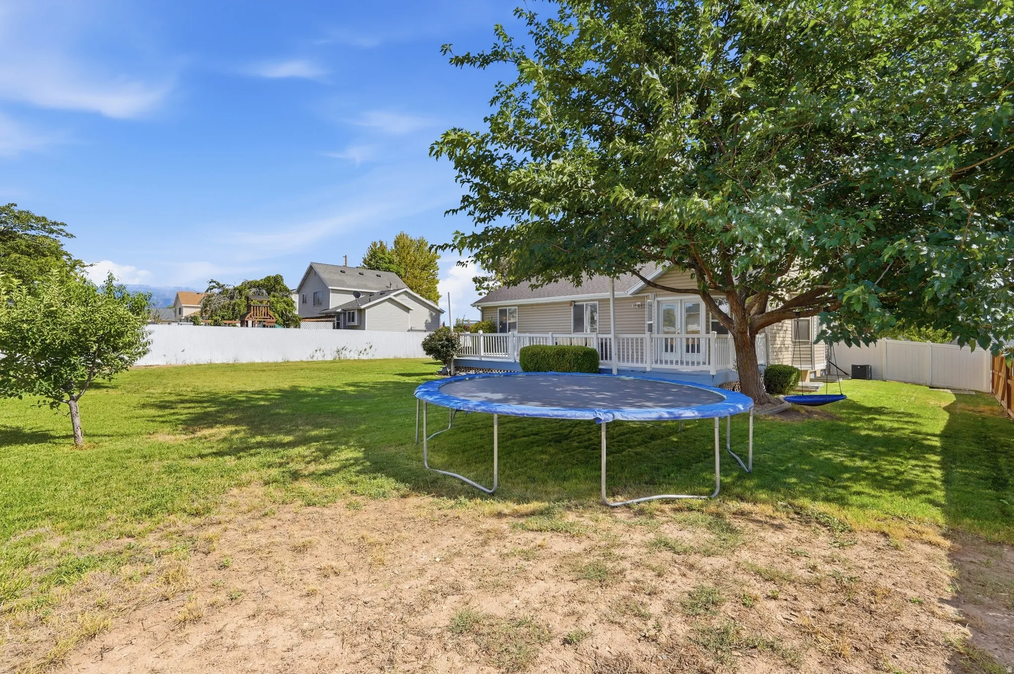 Expansive backyard featuring a manicured lawn, mature trees, and a white privacy fence