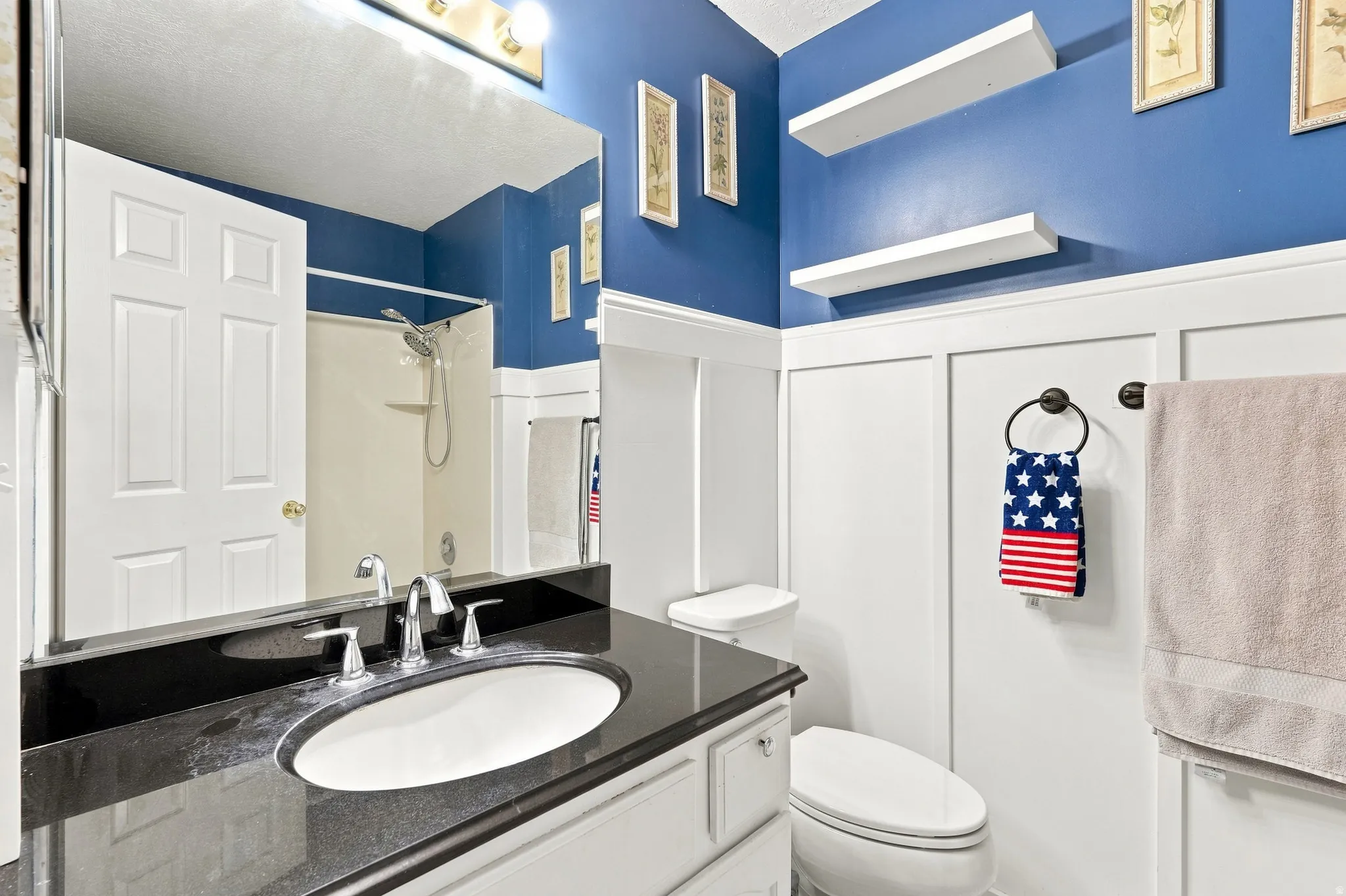 Vanity with black countertop and integrated sink, chrome faucet, wall-mounted mirror, and white floating shelves
