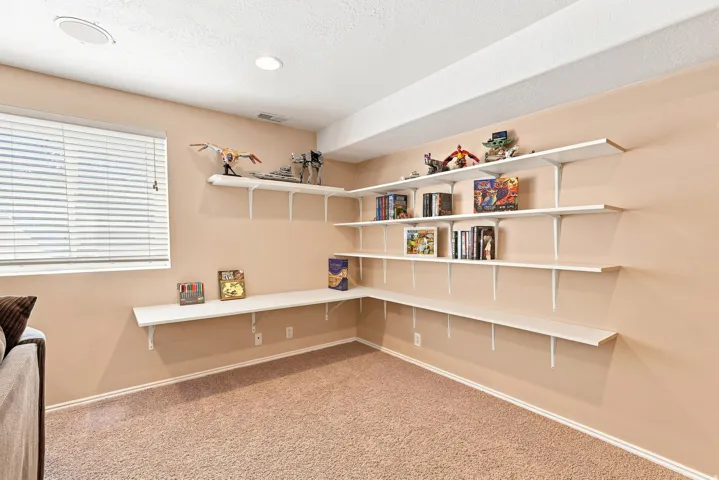 Wall-mounted shelving system, recessed ceiling lighting, textured carpeting, window with horizontal blinds, integrated ceiling speaker