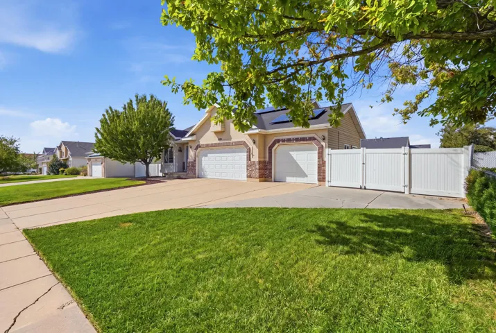 Tan stucco and brick exterior, two-car garage, white privacy fence, solar panels, and a concrete driveway