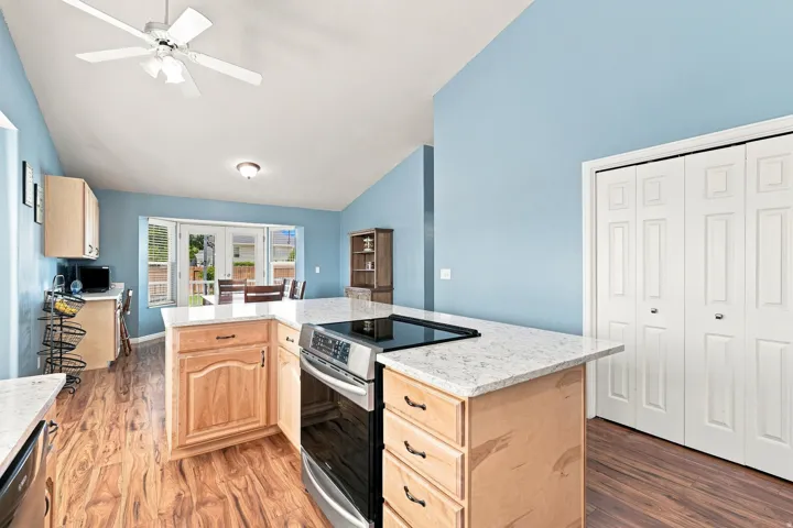 Kitchen island with built-in stainless steel range, light wood-finish cabinetry, light-colored countertops, wood-finish flooring, and vaulted ceiling
