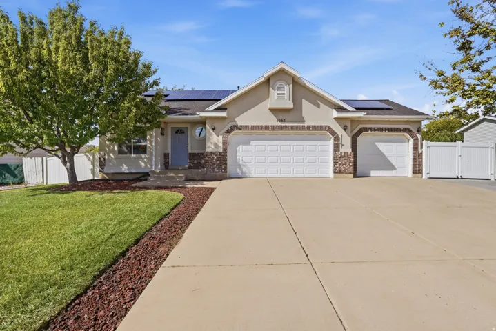 Stucco exterior with stone accents, integrated solar panels, a two-car garage, an additional single-car garage, and a concrete driveway