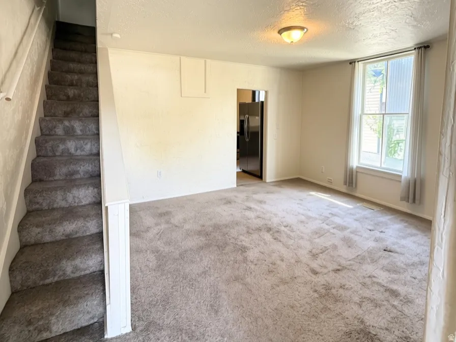 Carpeted flooring, a staircase with railing, and a window with natural light