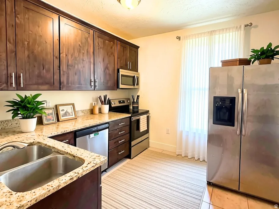 Kitchen featuring wood-finish cabinetry, granite countertops, stainless steel appliances, a double basin sink, and tile flooring
