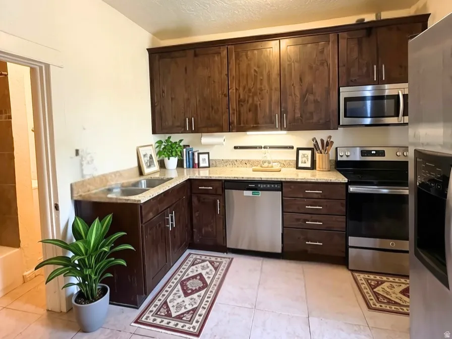 Kitchen featuring wood-finish cabinetry, stainless steel appliances, a corner sink, Dishwasher, and granite countertops