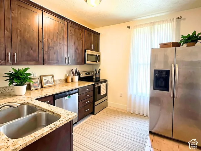 Kitchen featuring wood-finish cabinetry, granite countertops, stainless steel appliances, a double basin sink, and tile flooring