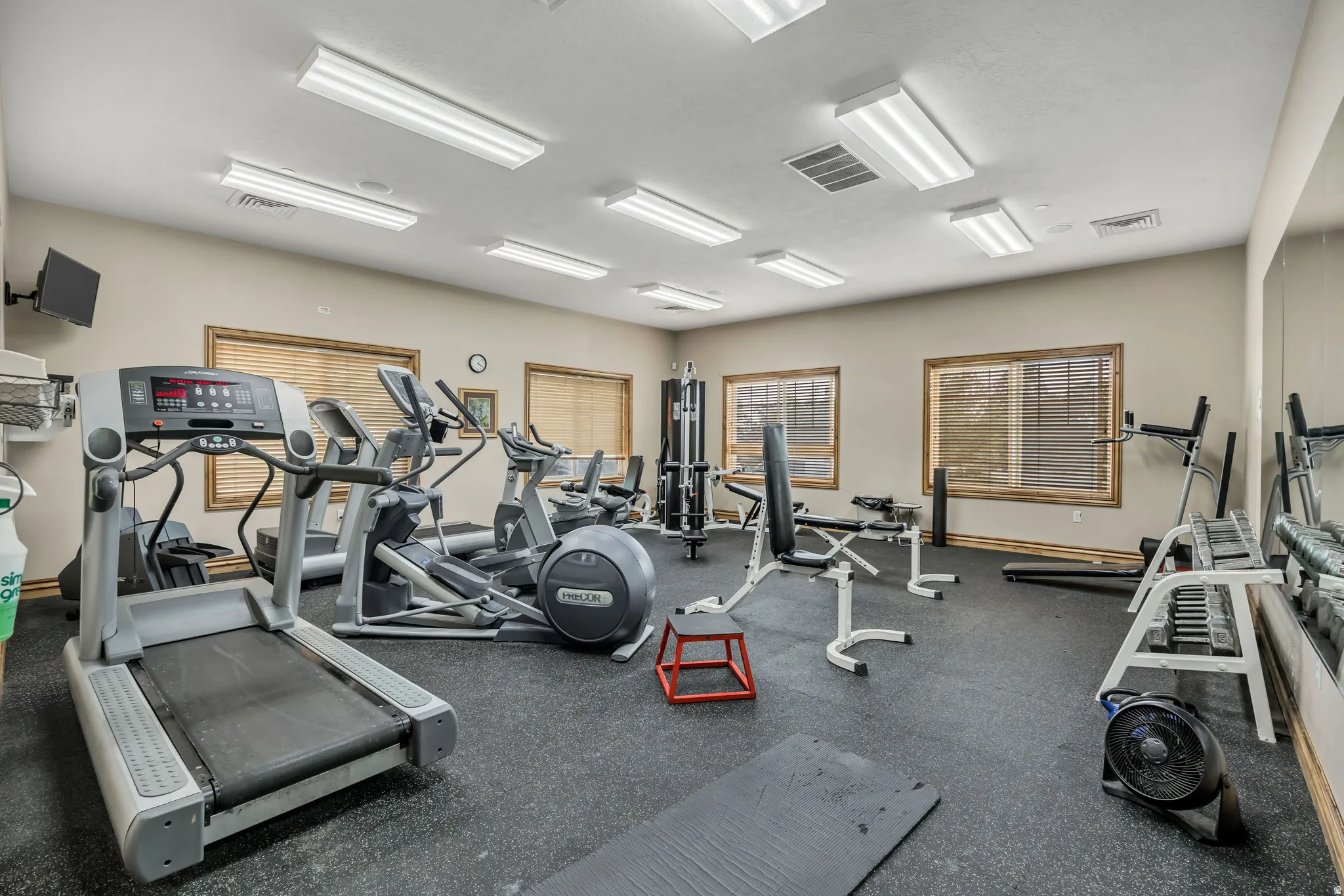Dedicated fitness space featuring rubber flooring, multiple windows with blinds, mirrored wall, and recessed fluorescent lighting