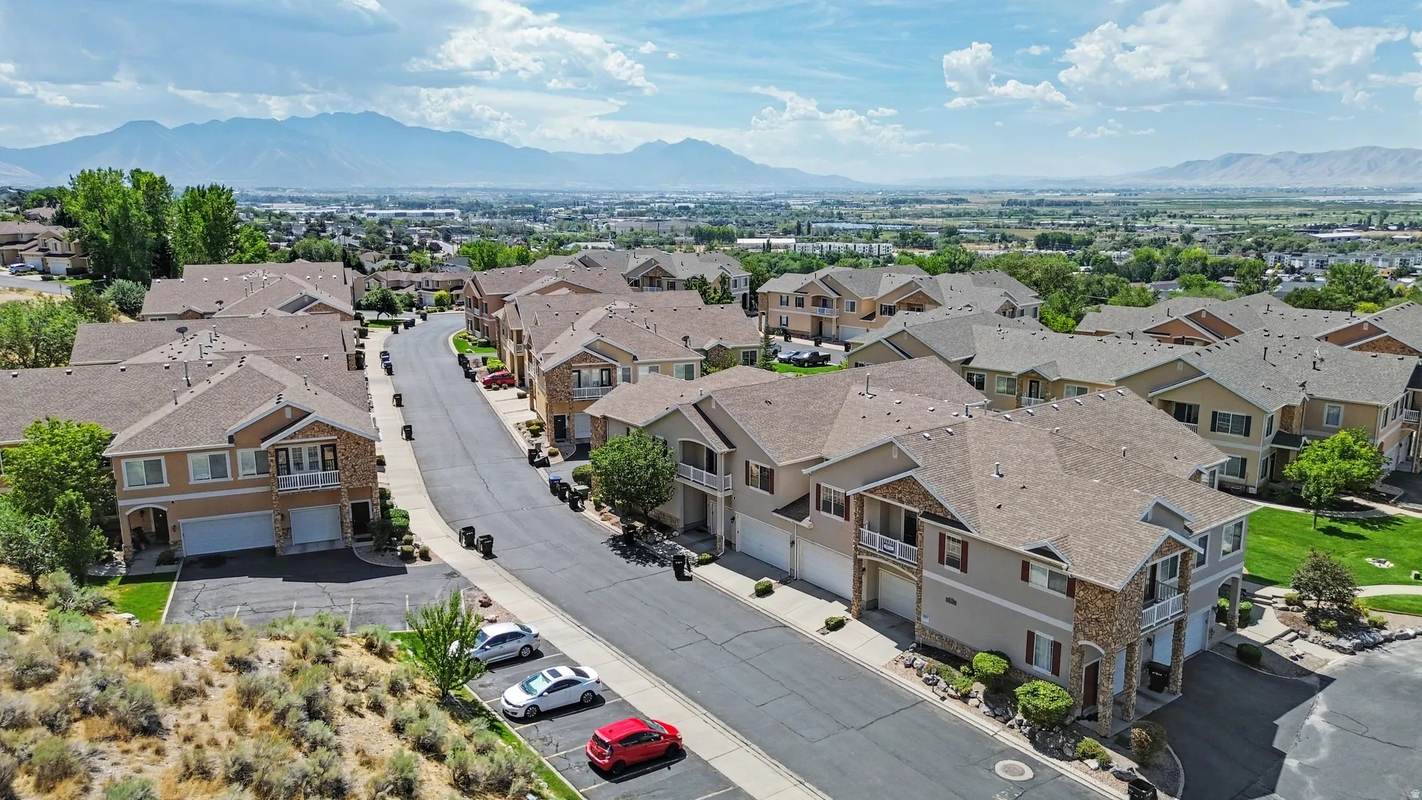 Community of multi-level residences with stone accents, attached garages, and a paved street