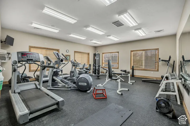 Dedicated fitness space featuring rubber flooring, multiple windows with blinds, mirrored wall, and recessed fluorescent lighting