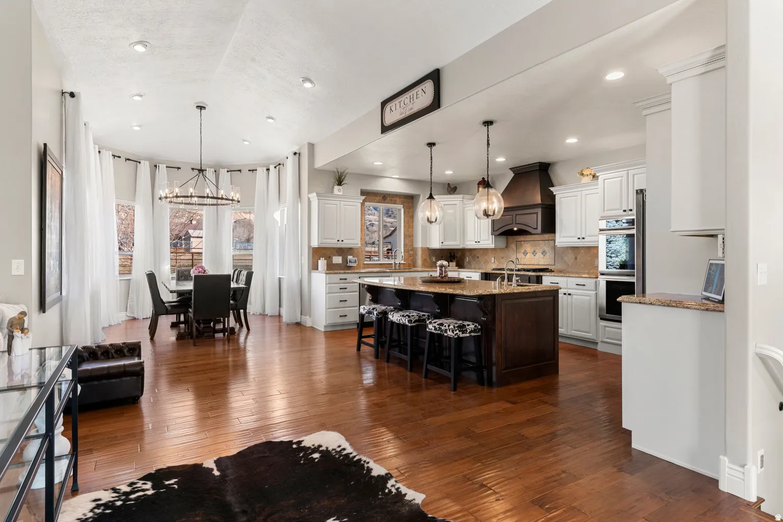 Hardwood-finish flooring throughout, kitchen with white cabinetry and a central island, recessed lighting, double wall oven, and a dining area with a bay window