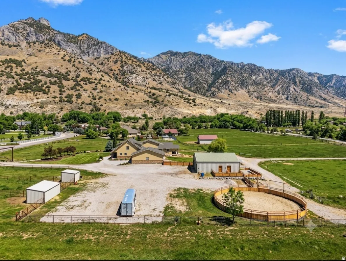 Expansive property featuring a residence, gravel parking area, multiple outbuildings, and a round pen, all set against a mountainous backdrop