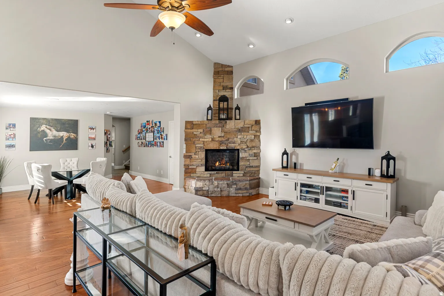 Vaulted ceiling with a ceiling fan, stone-clad fireplace, wood-finish flooring, and arched window details