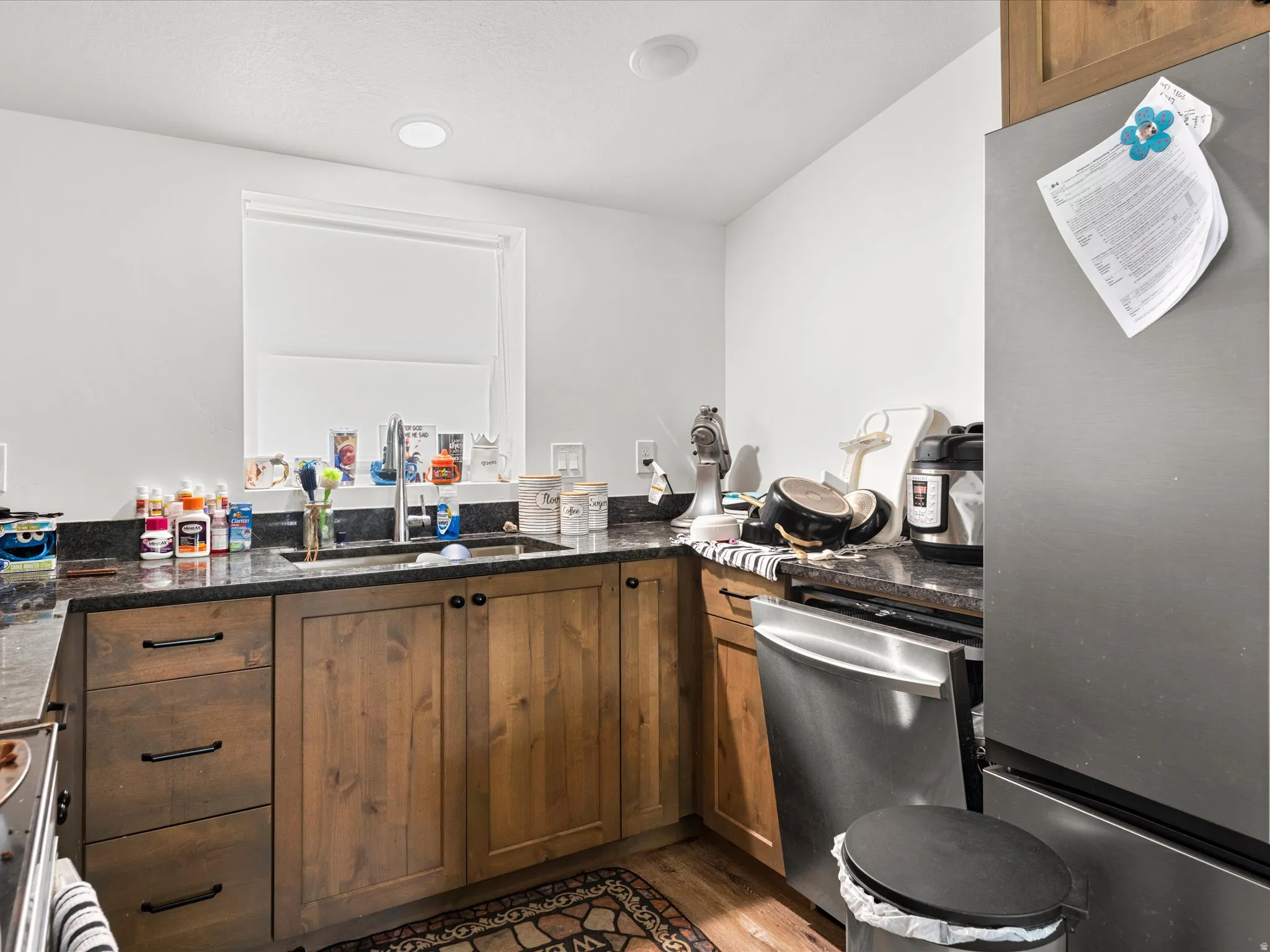 Wood-finish cabinetry with dark hardware, dark speckled countertops, stainless steel appliances, and a stainless steel sink with a gooseneck faucet