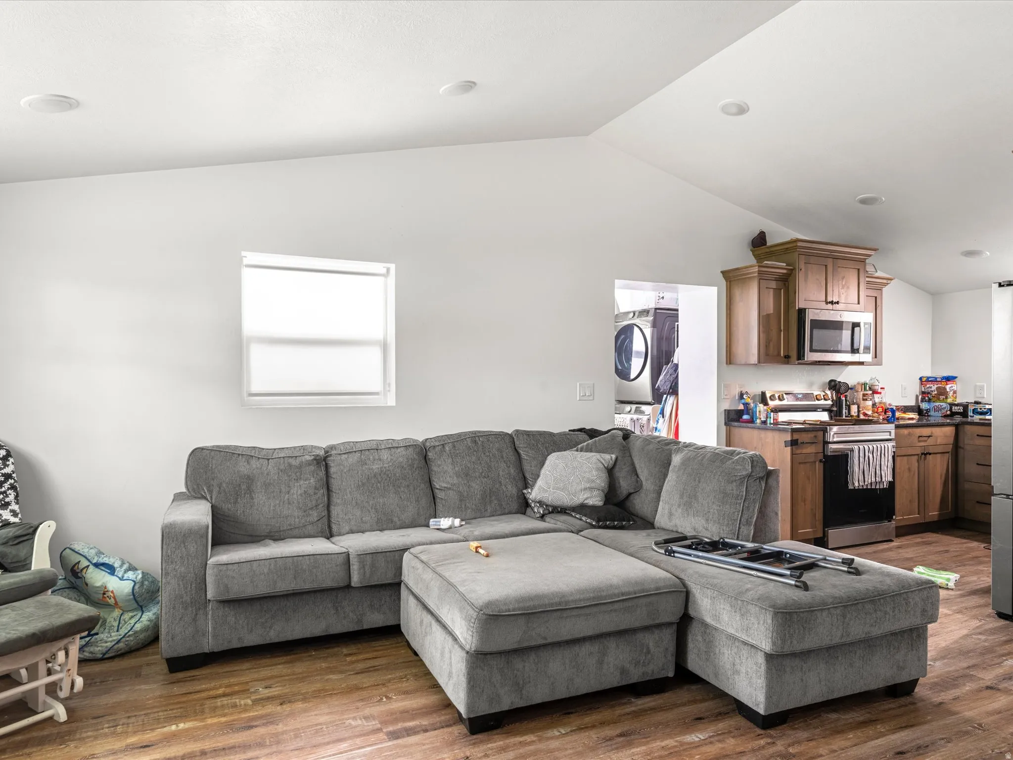 Vaulted ceiling with recessed lighting, wood-finish flooring, kitchen featuring wood cabinetry, stainless steel appliances, and dark countertops