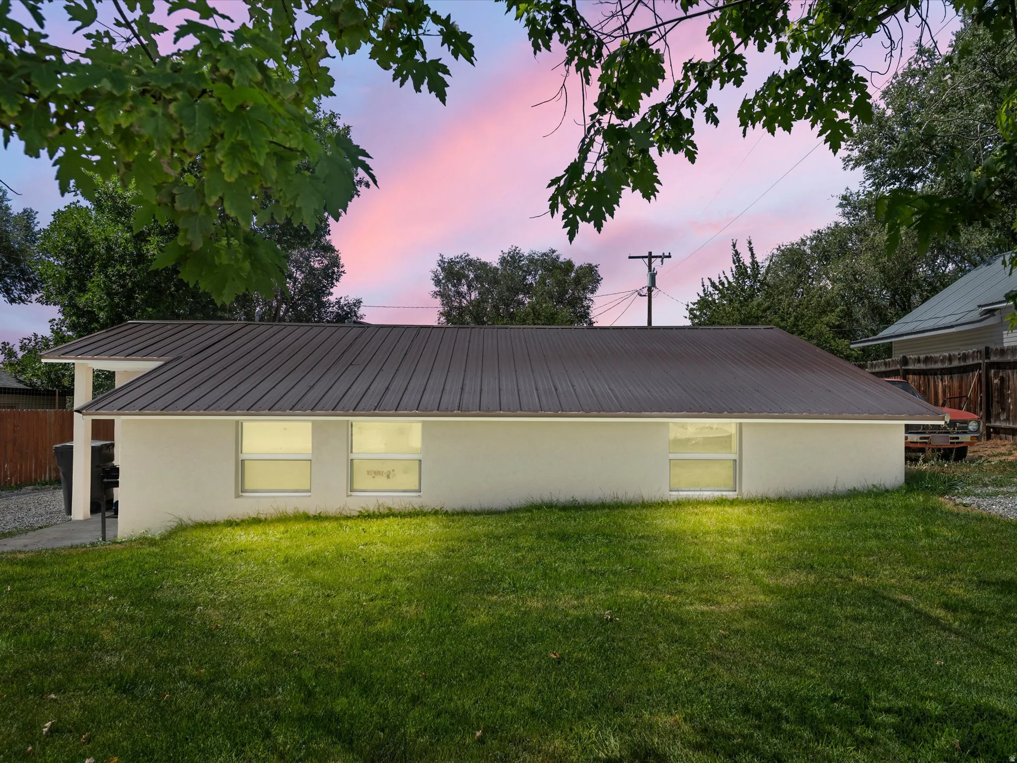 Metal roof, white exterior, multiple windows, covered porch structure, and a green lawn