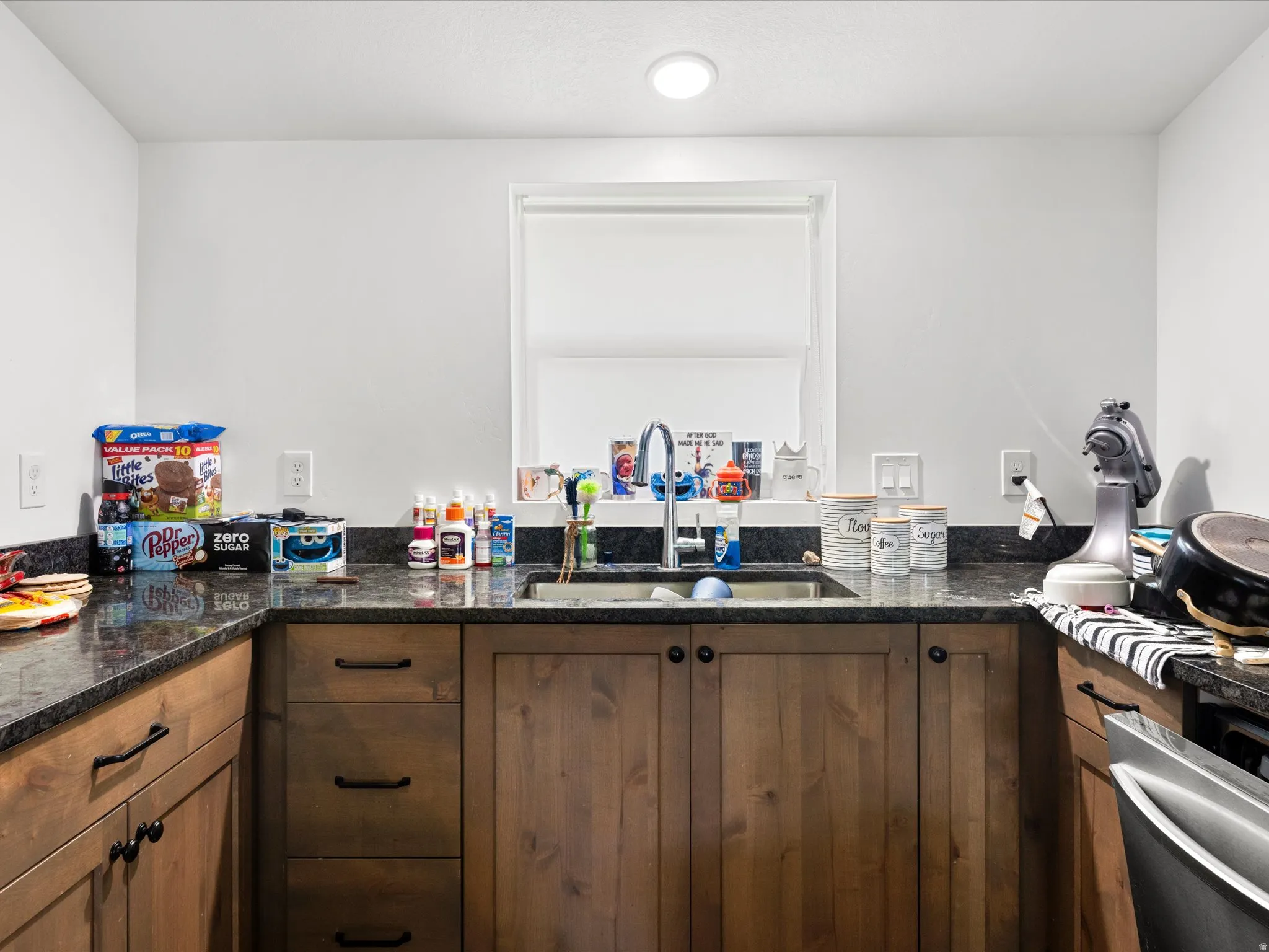 Stain-grade wood cabinetry with black hardware, dark stone countertops, stainless steel sink with gooseneck faucet, and recessed ceiling lighting