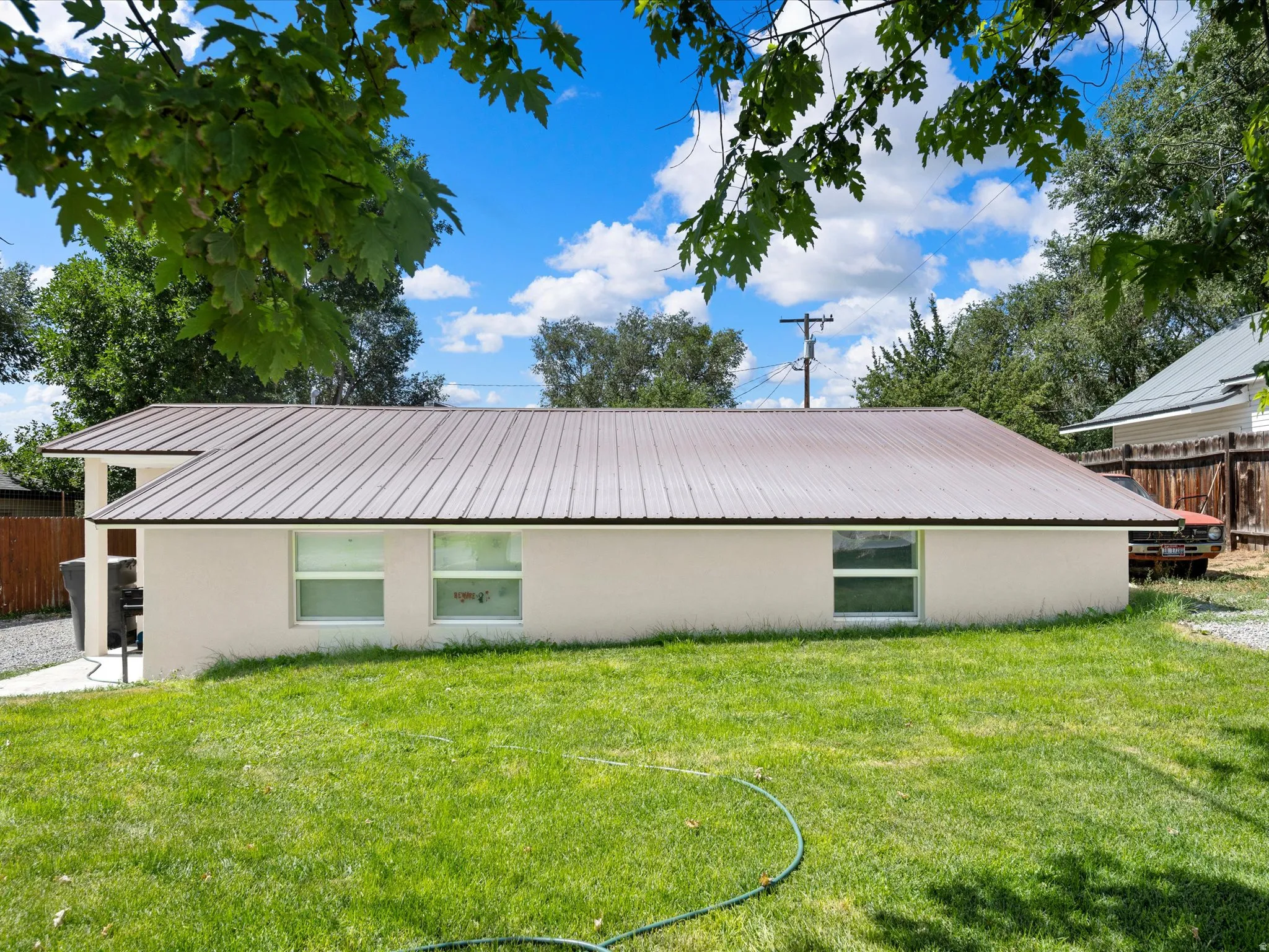 Expansive green lawn with a brown metal roof, light-colored exterior siding, and multiple windows