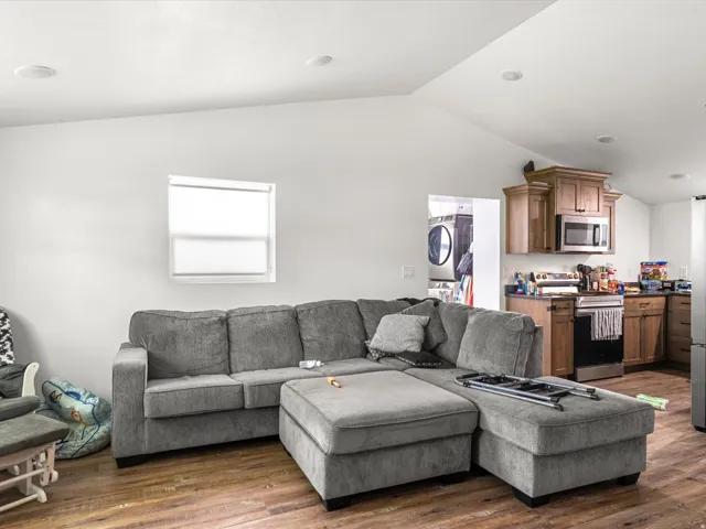 Vaulted ceiling with recessed lighting, wood-finish flooring, kitchen featuring wood cabinetry, stainless steel appliances, and dark countertops