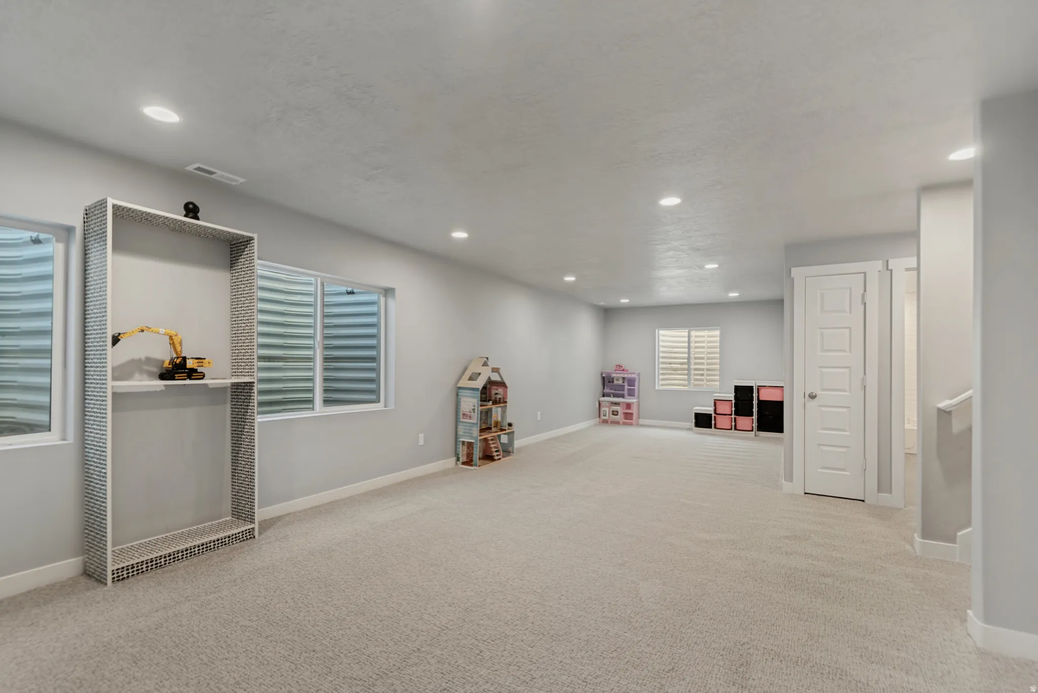 Expansive room featuring recessed lighting, light-toned carpeting, multiple windows, and a built-in shelving unit