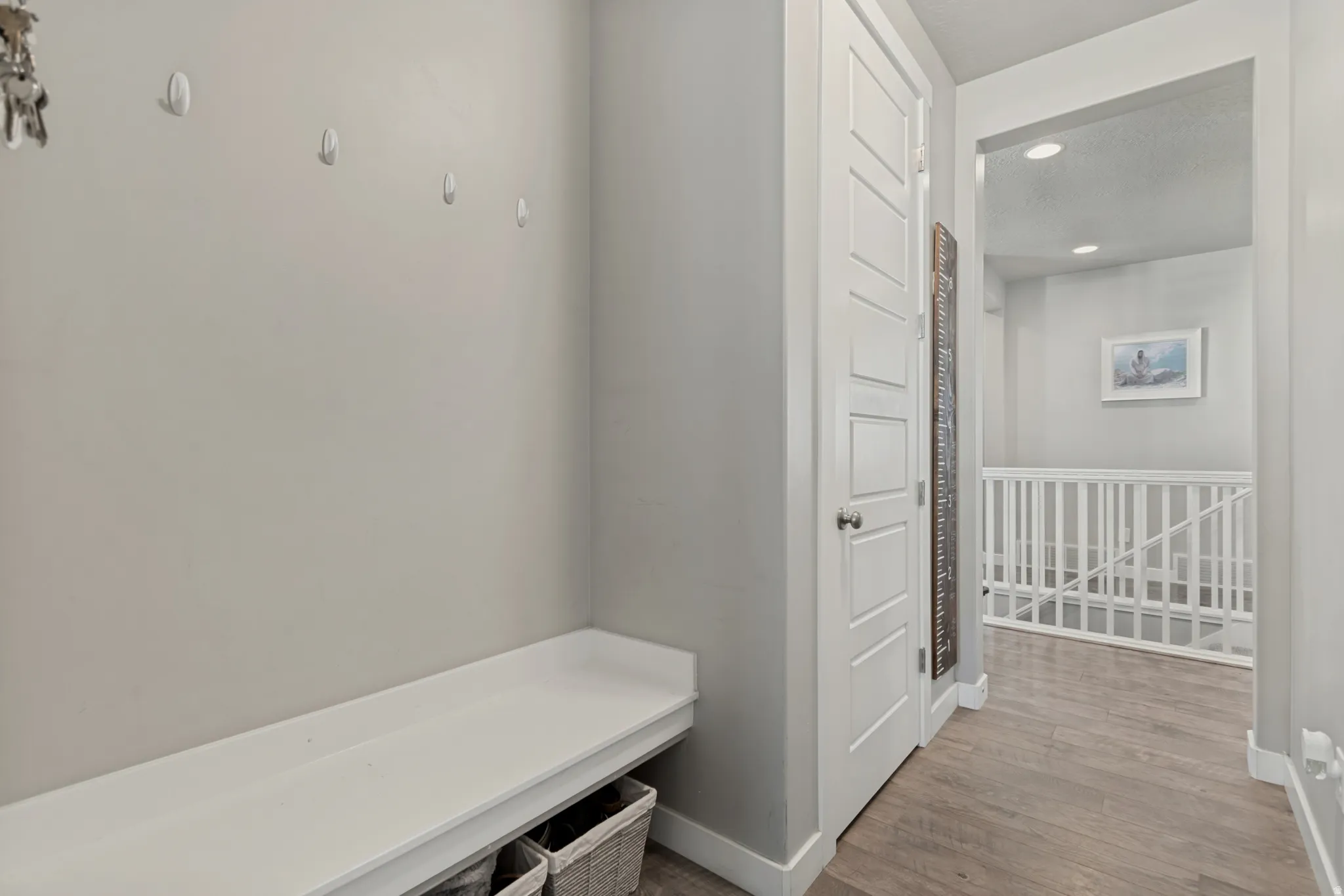 Built-in bench with storage, wood-finish flooring, white panel door, recessed lighting, and white stair railing