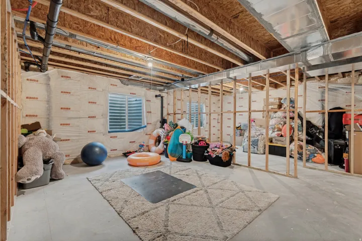Unfinished basement featuring exposed wood joists, concrete flooring, and an egress window