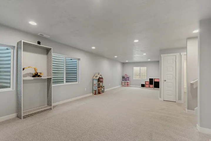 Expansive room featuring recessed lighting, light-toned carpeting, multiple windows, and a built-in shelving unit