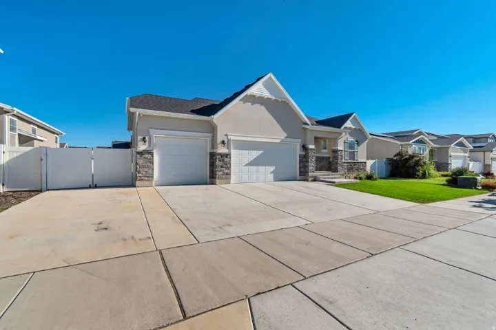 Stucco exterior with stone accents, two-car garage, multiple gables, and a white privacy fence