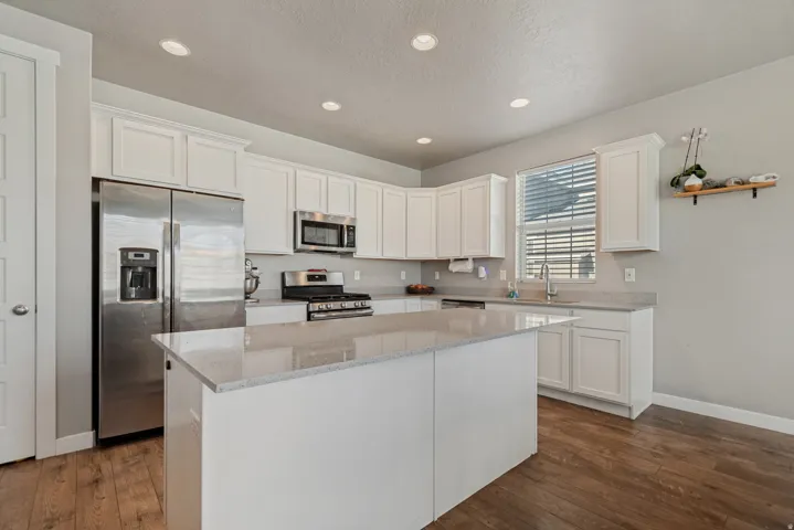 Kitchen featuring white cabinetry, light-toned countertops, stainless steel appliances, a center island, and wood-finish flooring