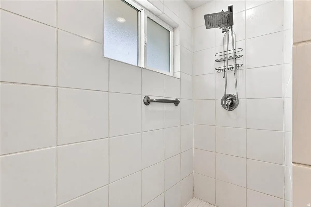 White tiled shower with a frosted window, chrome grab bar, and a rainfall showerhead with an integrated caddy