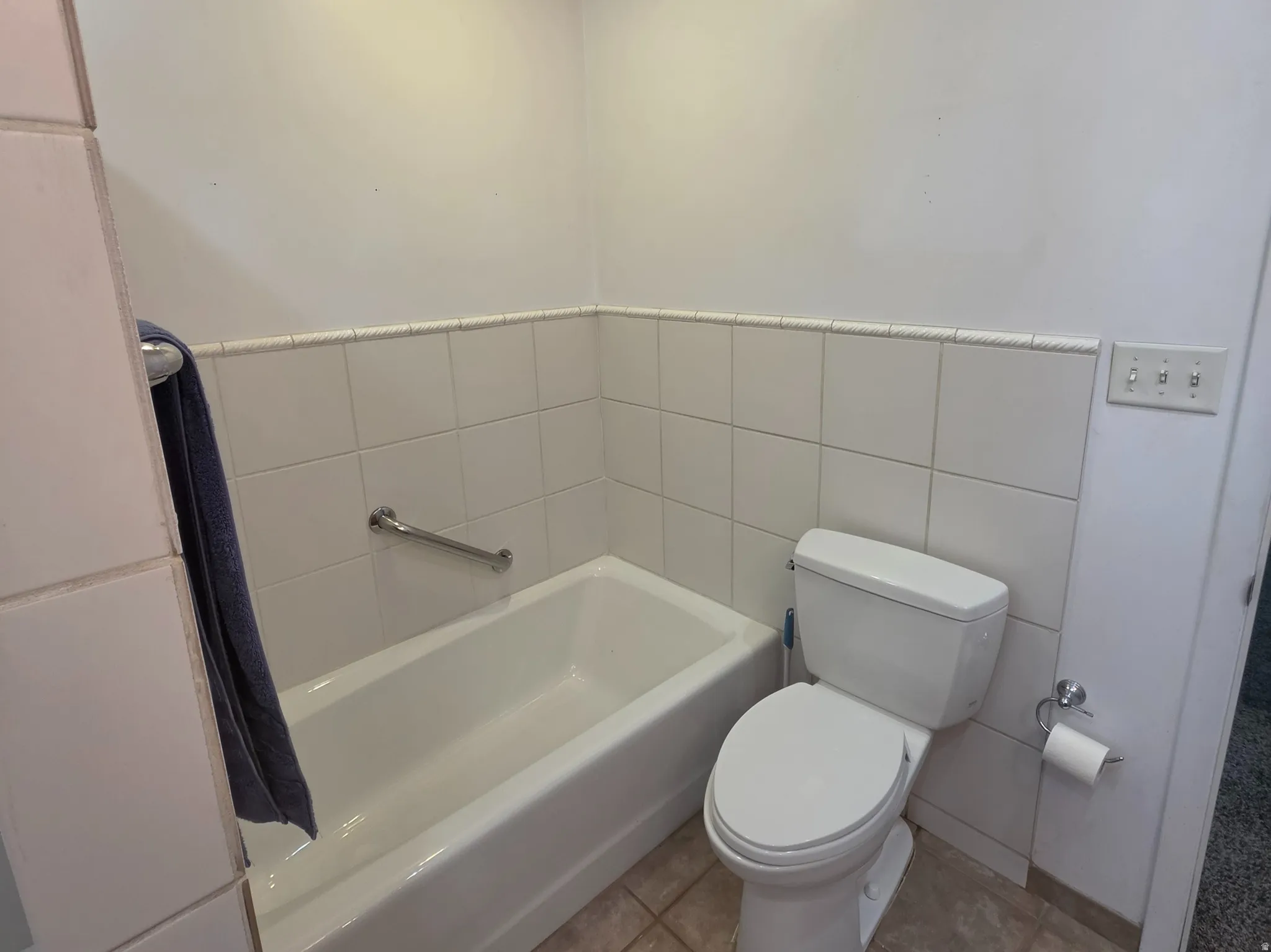 Recessed ceiling lighting, white ceramic wall tile, built-in bathtub, grab bar, and floor tile