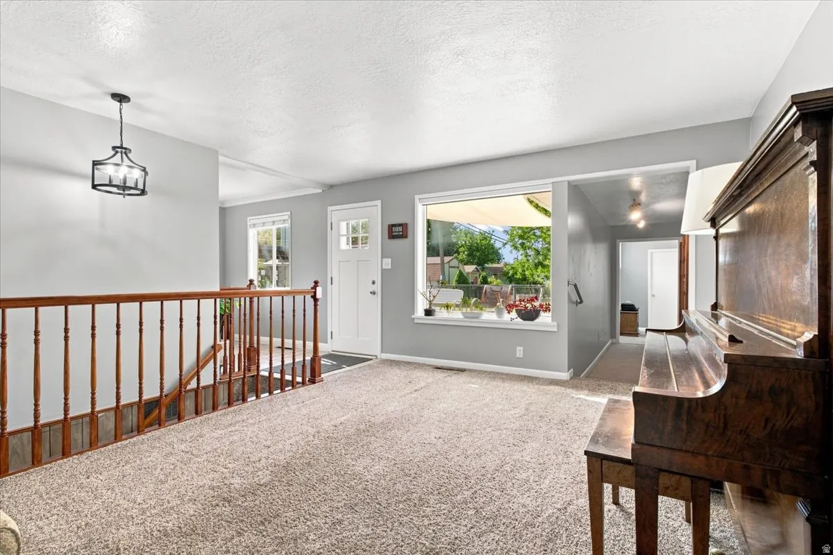 Carpeted flooring, contemporary chandelier, wood railing, large window, and white paneled door