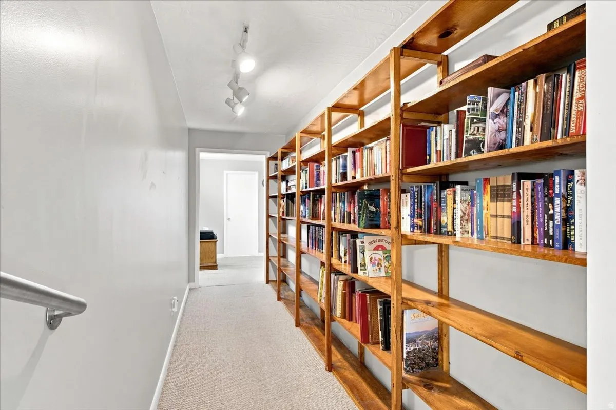 Hallway featuring extensive wood-finish shelving, track lighting, and a neutral carpet