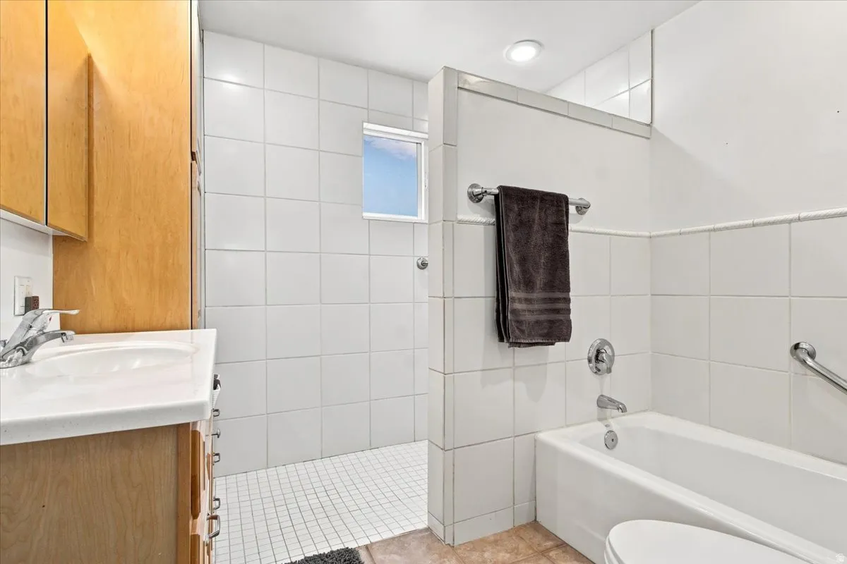 Full bathroom featuring a white tile shower with a small window, a separate bathtub, a vanity with wood-finish cabinetry, and a white countertop with an integrated sink