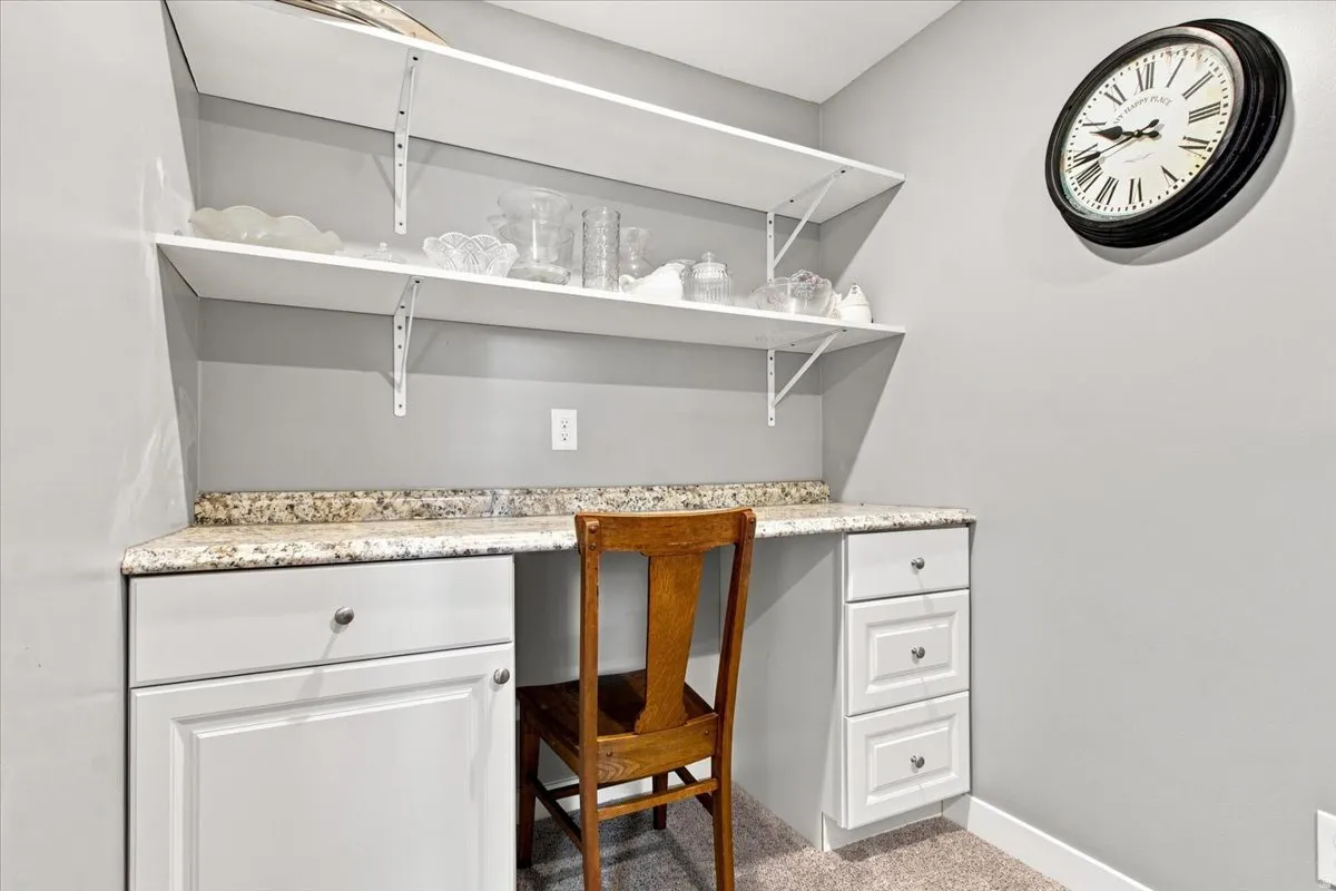 Built-in desk area featuring a light-toned countertop, white cabinetry with silver-toned hardware, and open white shelving
