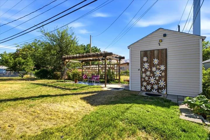 Expansive backyard with a wood pergola, detached shed featuring a unique decorative door, and a partially fenced perimeter